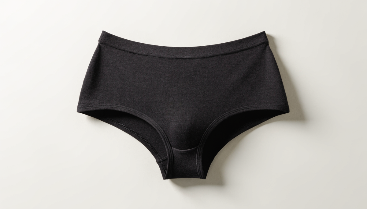 Culotte menstruelle noire taille haute posée à plat sur un fond clair